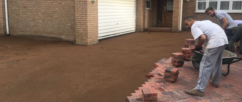 Two of the crew laying a brick edge course by hand on a screeded sand bed